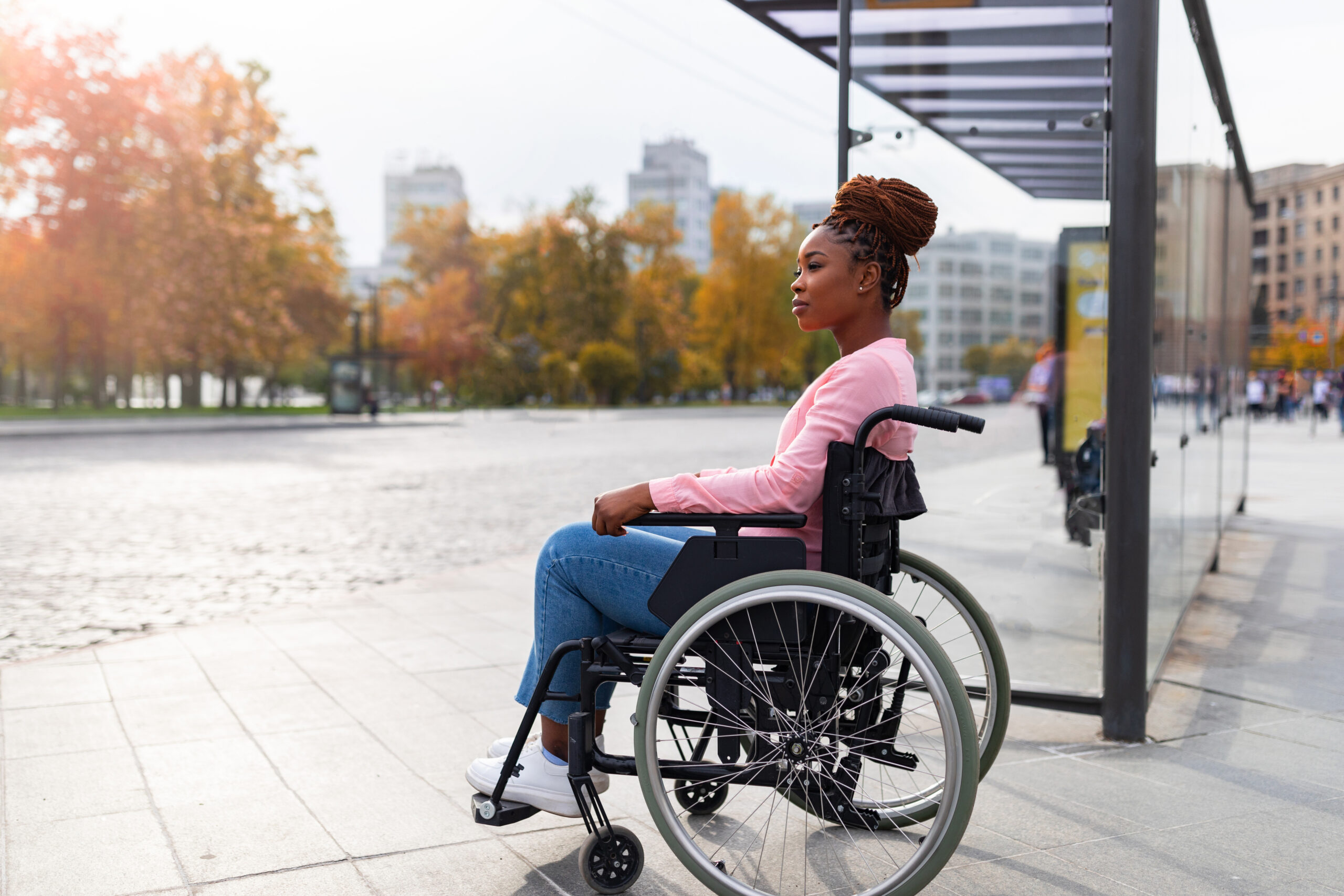A woman in a wheelchair waiting at a bus station, representing inclusive travel solutions from a holiday company for disabled people.