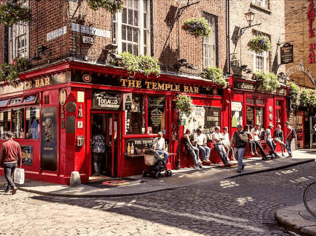 The Temple Bar, a vibrant red pub in Dublin, bustling with patrons outside and adorned with hanging plants, showcasing local culture and nightlife.