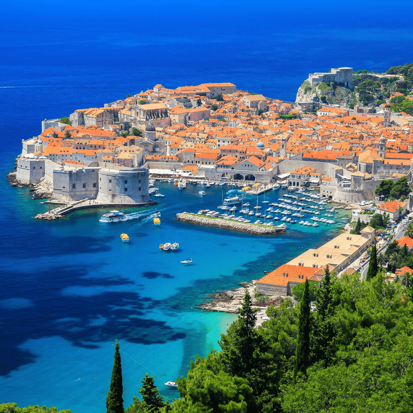 Aerial view of Dubrovnik, Croatia, showcasing its historic architecture, orange-roofed buildings, and vibrant blue waters of the Adriatic Sea.