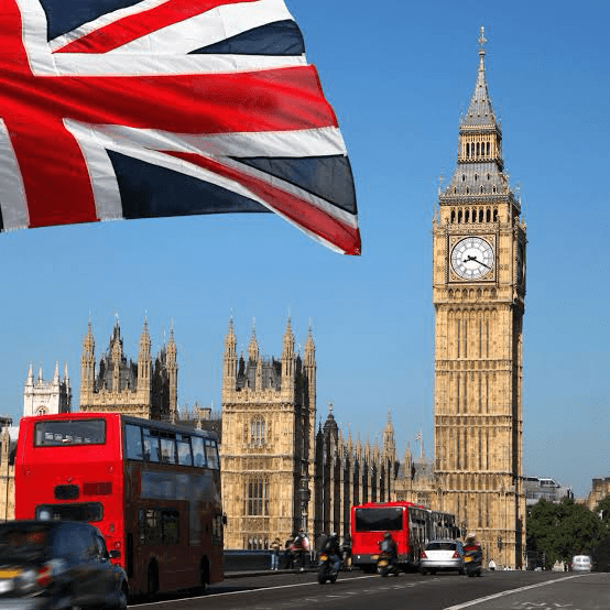 Union Jack flag in the foreground with Big Ben and the Houses of Parliament in the background. The image captures iconic symbols of London and British culture.