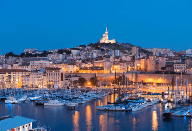 Vibrant nighttime view of Marseille's harbor, featuring illuminated yachts and the iconic Notre-Dame de la Garde on the hilltop.