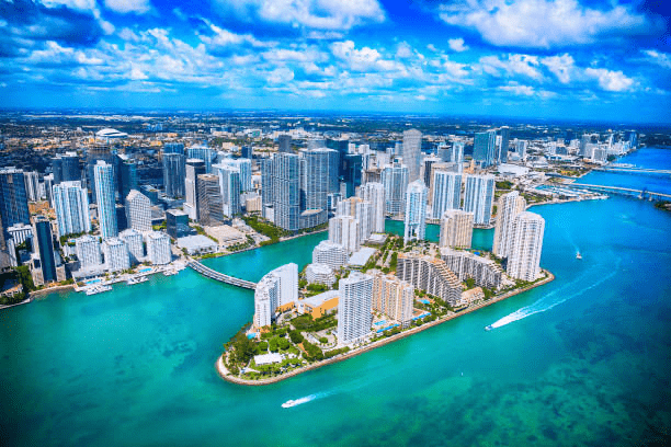 Aerial view of Miami's vibrant skyline, with high-rise buildings lining a turquoise waterfront, showcasing a bustling coastal cityscape.