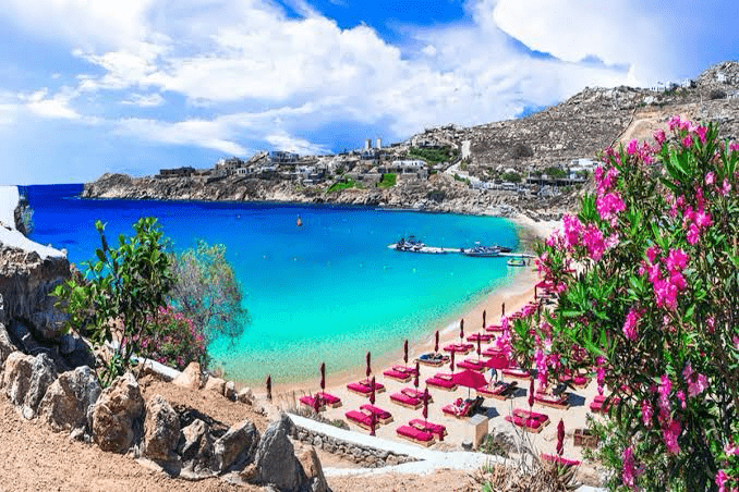 Turquoise waters and sandy beach dotted with red loungers and umbrellas, framed by lush greenery and a scenic coastal view. Perfect for relaxation.