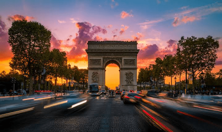 Arc de Triomphe at sunset, framed by vibrant clouds and bustling traffic, captures the intersection of history and modern Parisian life.