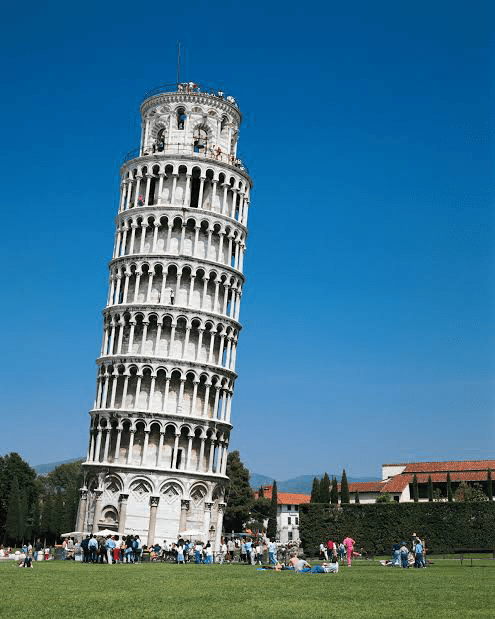 Leaning Tower of Pisa, a renowned architectural landmark, attracts visitors enjoying the lush green lawn and clear blue sky.