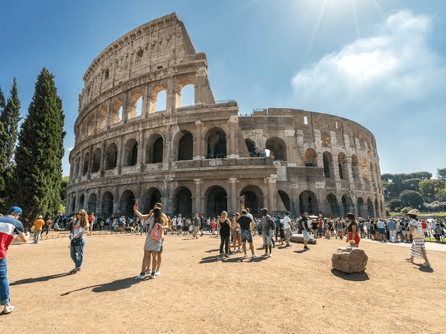 The Colosseum in Rome, an iconic ancient amphitheater, surrounded by a large crowd of tourists enjoying the historic site under bright sunlight.