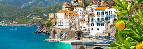 Ceramic white houses with orange roofs cling to rocky cliffs above a turquoise sea, framed by vibrant lemon trees, showcasing Amalfi's coastal charm.