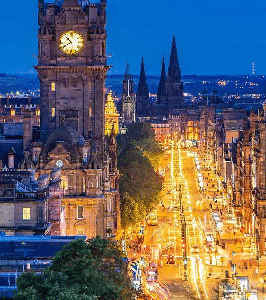 Edinburgh's skyline at dusk features the iconic clock tower, vibrant street lights, and spires of nearby churches, showcasing the city's charm.