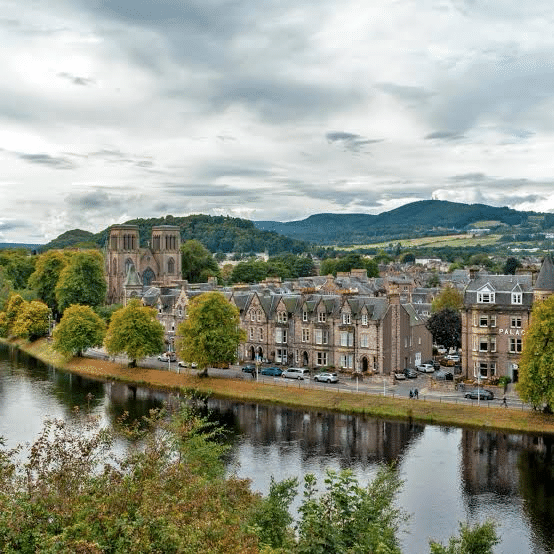 Scenic view of Inverness, Scotland, featuring historic buildings along the River Ness with lush green hills in the background.