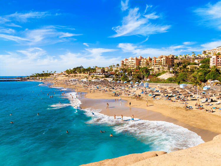 Crowded beach scene in Cabo San Lucas, Mexico, with sunbathers, swimmers, and resorts under a clear blue sky. Summertime leisure and relaxation.